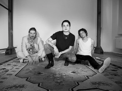 Schwarz-weiß-Foto der Band Sinem, vor weißem Hintergrund, sitzend bzw. kniend auf einem Teppich posend.