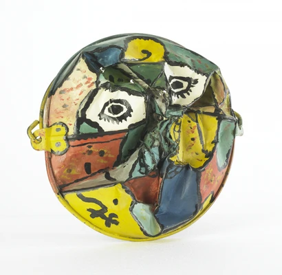 Runde, bunt glasierte Keramikskulptur mit abstrakten, mehrfarbigen Formen und Linien. Die Oberfläche ist stark verformt und eingedrückt, sodass eine unregelmäßige Struktur entsteht. Zu sehen sind leuchtende Farbfelder in Gelb, Rot, Grün und Blau sowie zwei schwarze, stilisierte Augenformen