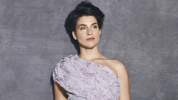 Frau in elegantem hellviolettem Kleid vor einer grauen Wand