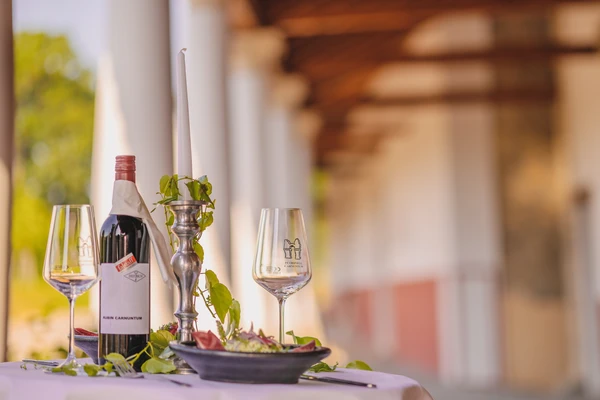 Wine bottle and wine glasses on a set table with candlestick and vine leaves as decoration. In the background, you can see the white columns of Roman buildings.