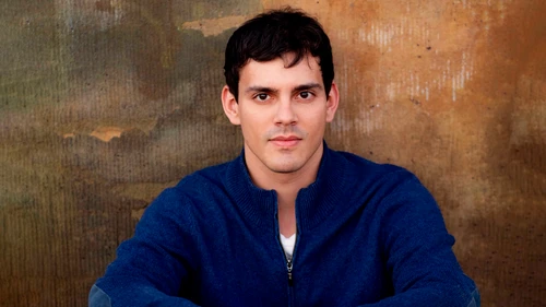 Junger Mann in blauem Pullover sitzt an einer alten Holzmauer