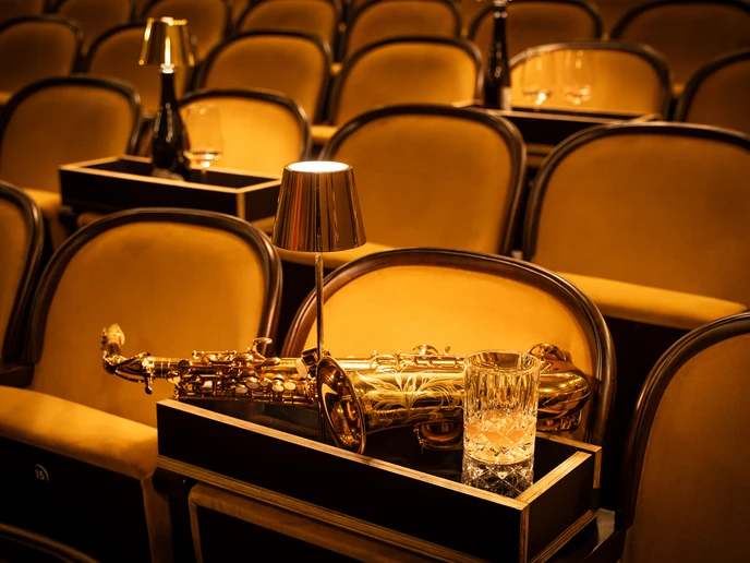 Saxophon, Lämpchen, Glas auf einem Tischchen in bernsteinfarbenen Sesselreihen