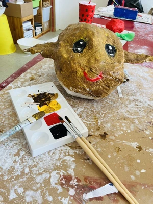 Pappeskulptur mit langen Ohren und angemalt. Vorne sind Pinsel und Farben zu sehen.