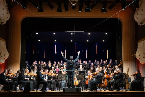 Orchester, Dirigent und Sänger musizieren auf einer Bühne