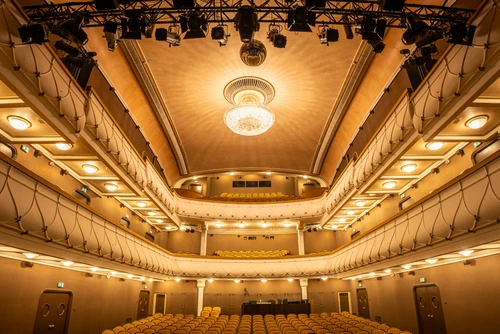 Theatersaal mit bernsteinfarbener Bestuhlung, Kristallluster, der Lichter an die Decke wirft