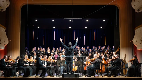 Orchester, Dirigent und Sänger musizieren auf einer Bühne