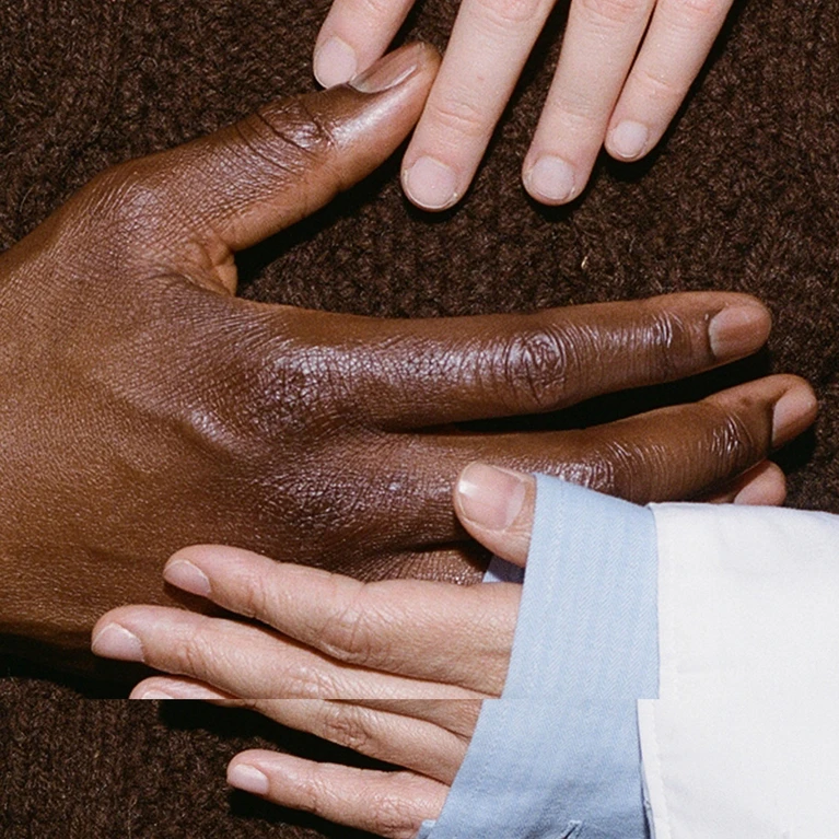 The theme for the Festspielhaus’s 2026/2027 season. The image shows hands touching, set against a very dark brown background that matches the colour of a person’s jumper.