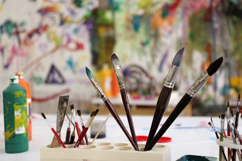 Brushes and paints in front of a painted wall in the atelier