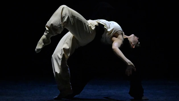 Performancefoto der Choreografie "Frontier" von Crystal Pite. Zu sehen ist ein:e Tänzer:in des Ballet BC weißgekleidet in einer dynamischen Tanzbewegung vor schwarzem Bühnenhintergrund.