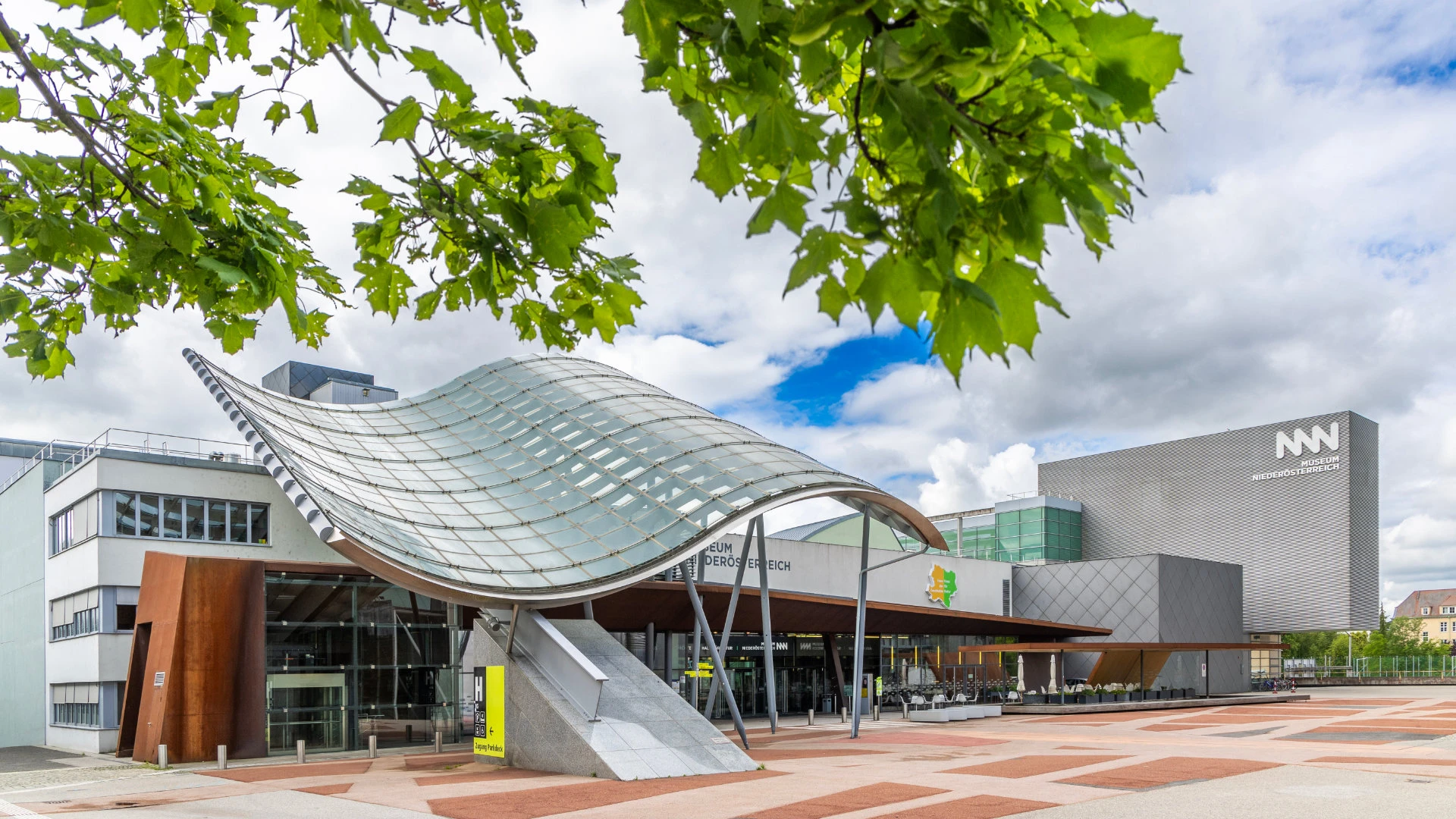 Eingangsbereich des Museum Niederösterreich mit geschwungenem Glasdach und moderner Architektur.