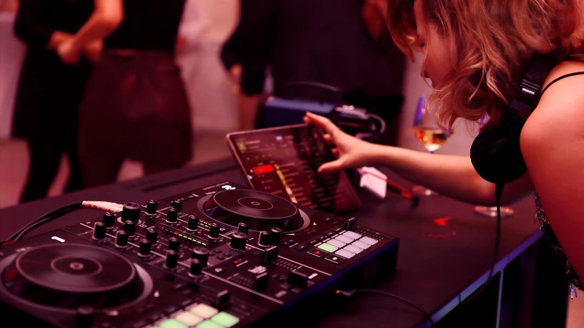 Turntables werden von DJ Rambo Schmidt bedient. Im Hintergrund tanzen Besucher*innen.