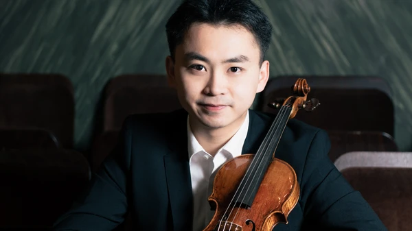 Mann mit Anzug sitzt mit einer Violine zwischen Stühlen