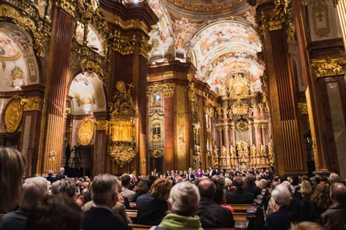 Innenansicht einer prunkvollen Barockkirche während eines Konzerts, mit üppiger Vergoldung und Deckengemälden.