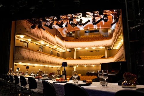 Lange Tafel auf einer Theaterbühne, dahinter Zuschauerraum, Gläser, Gedecke