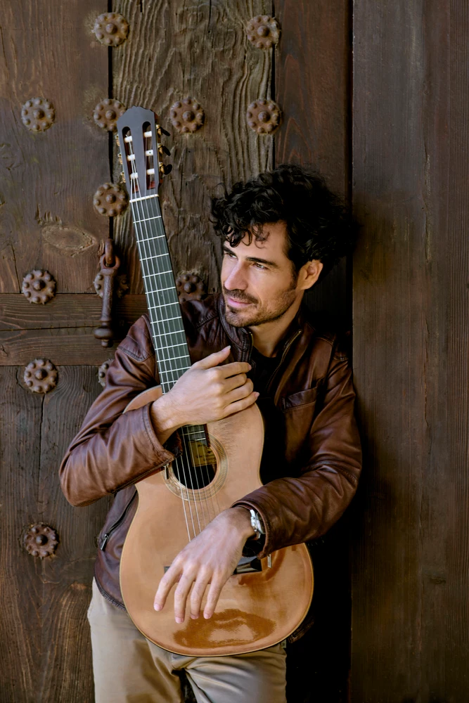 Pablo Sainz-Villegas mit Gitarre lehnt an einem großen Holztor