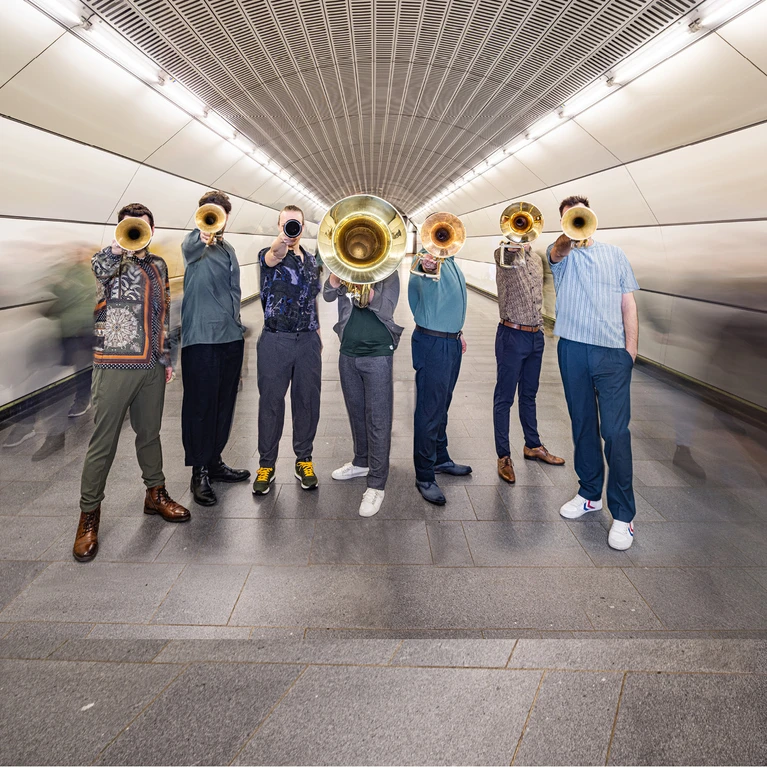 Gruppenfoto vom Bläserensemble "Federspiel", aufgenommen im Schacht einer U-Bahnstation. Die Musiker halten ihre Instrumente nach vorne.