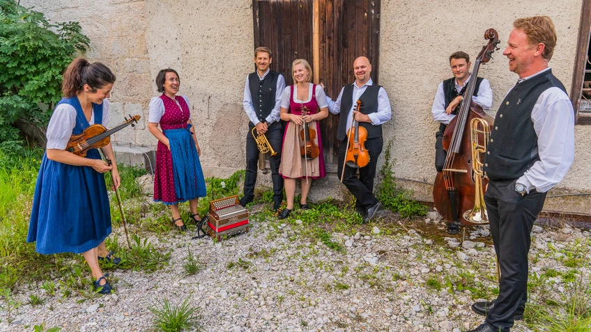 Musikgruppe in Tracht mit Instrumenten im Schotter vor einem alten Gebäude
