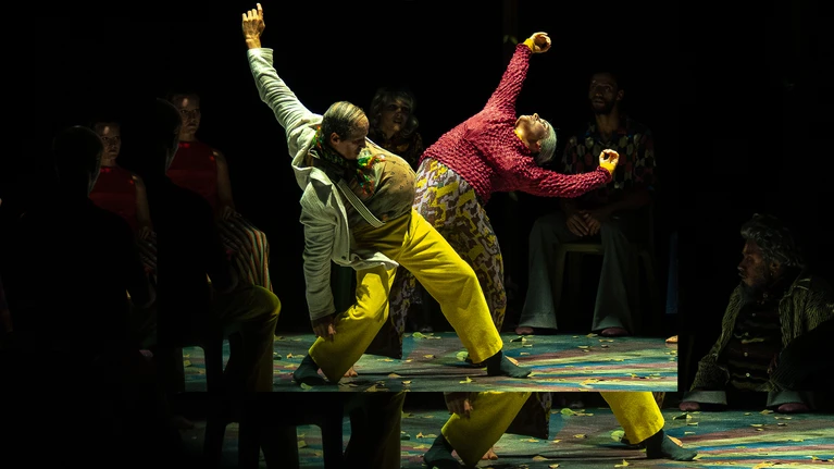 Zwei Tänzer:innen der Compagnie Käfig tanzen in Kostümen, die sie älter aussehen lassen sollen in dem Stück "Beauséjour", beide stark zurückgelehnt ein Hohlkreuz bildend, mit den Kopf nach oben schauend.
