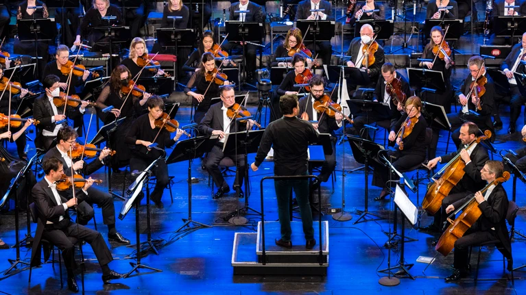 Herbert Pixner Projekt gemeinsam mit dem Tonkünstler-Orchester auf einer großen Bühne, Musiker mit traditionellen und klassischen Instrumenten.