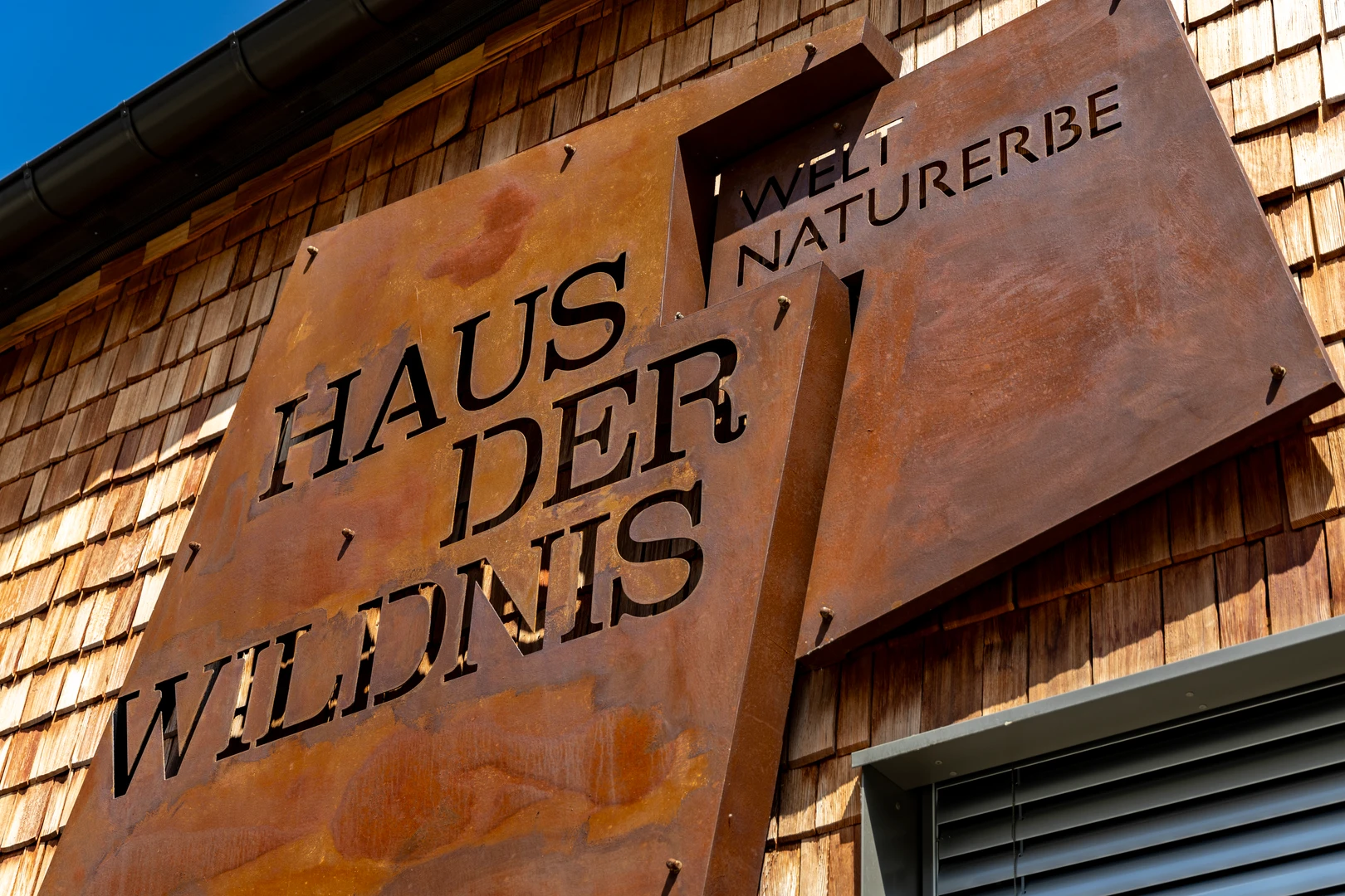 Logo aus Metall in rostiger Farbe auf der Außenfassade des Haus der Wildnis. 