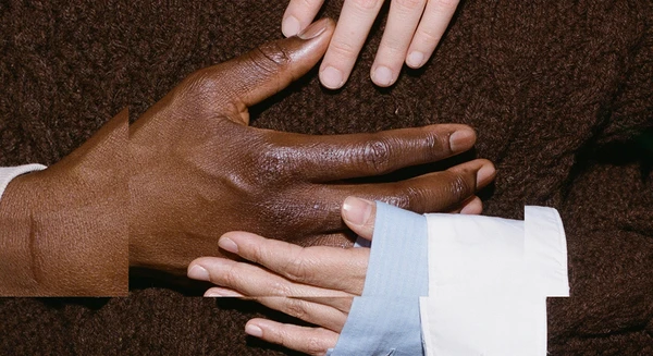 The theme for the Festspielhaus’s 2026/2027 season. The image shows hands touching, set against a very dark brown background that matches the colour of a person’s jumper.