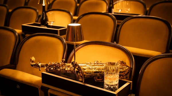 Saxophon, Lämpchen, Glas auf einem Tischchen in bernsteinfarbenen Sesselreihen