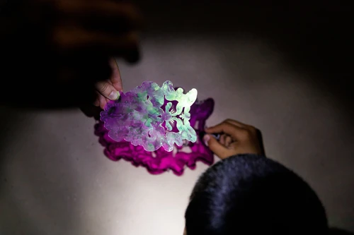 Children's hands hold a cut Plexiglas figure by Robert Gabris that casts a purple shadow on the background.