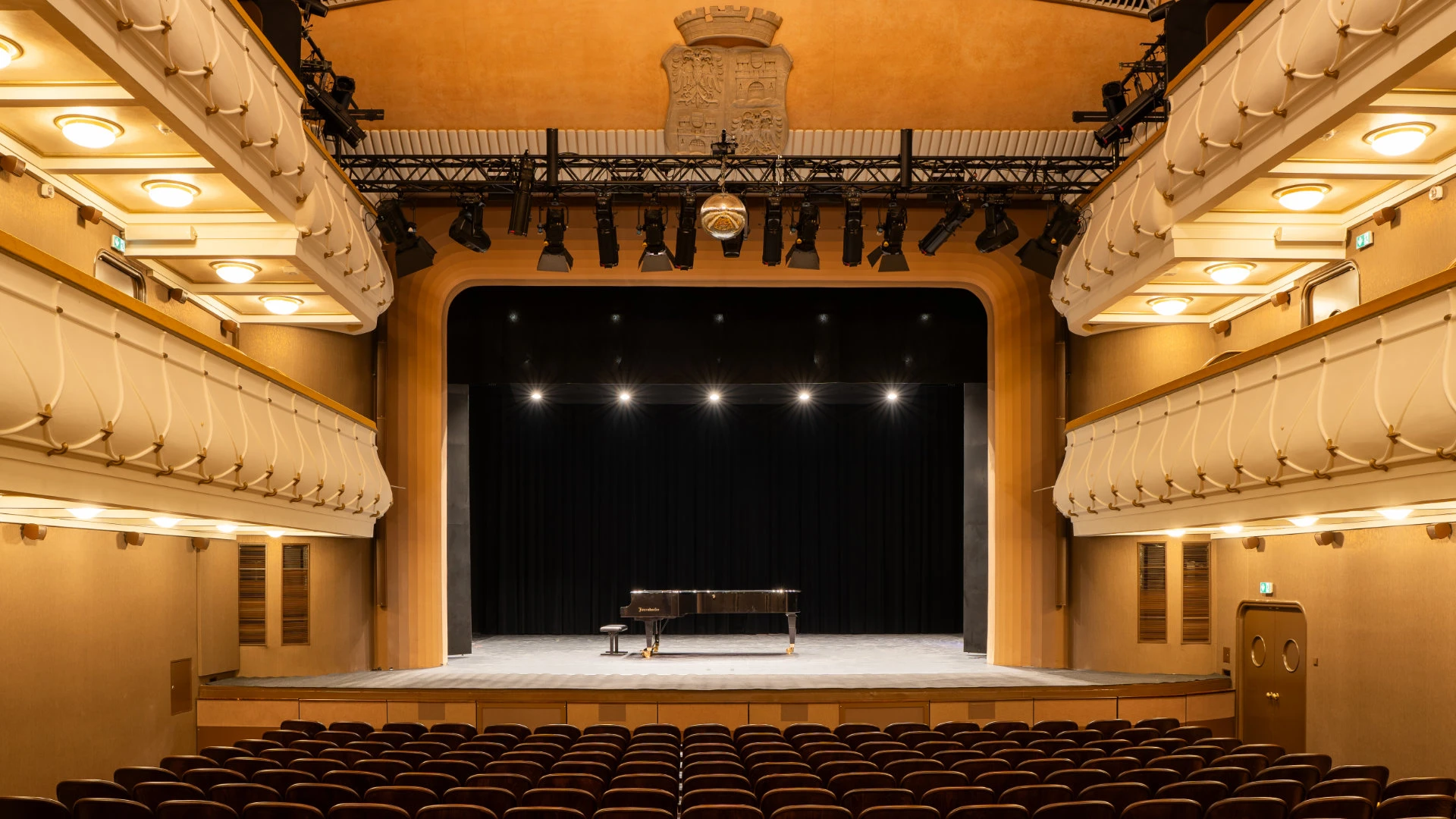 Innenansicht vom Stadttheater Wiener Neustadt mit leuchtend beleuchteter Bühne, schwarzem Vorhang und Konzertflügel.