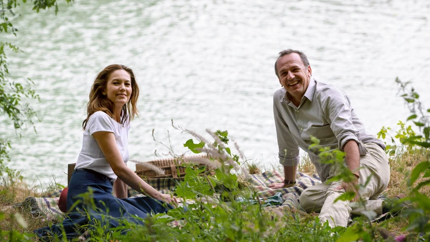 Ein Paar sitzt an einem See auf einer Picknickdecke im Grünen