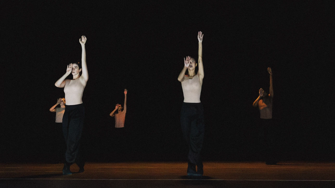 Performancefoto der Choreografie "SWAY" von Medhi Walerski. Zu sehen sind Tänzer:innen des Ballet BC, gekleidet in schwarzer Hose und weißem Shirt, vor schwarzem Bühnenhintergrund, in einer Gruppenchoreografie. 