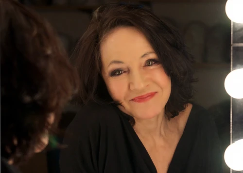 Maria Bill schaut aus dem Spiegel, dunkle Haare, roter Lippenstift