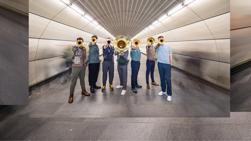 Group photo of the wind ensemble ‘Federspiel’, taken in the shaft of an underground station. The musicians are holding their instruments out in front of them.