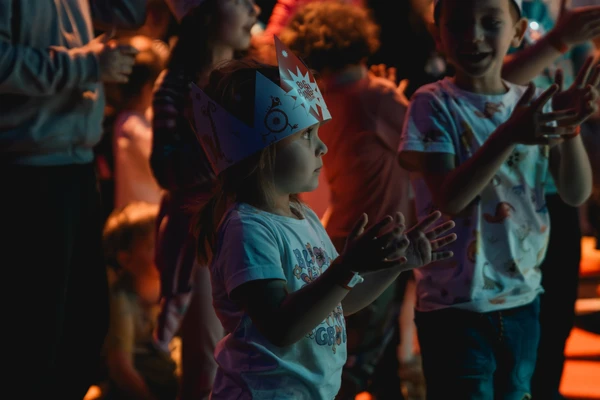 Stimmungsfoto vom "BIG BANG Festival - Musikabenteuer für junges Publikum"; ein Mädchen steht im Bildvordergrund mit einer "BIG-BANG"-Krone auf dem Kopf und klatscht in die Hände.