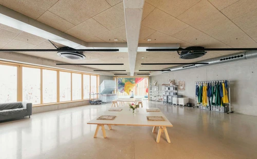 Handmade paper lies on tables. Colourful smocks hang in the background, you can see a drying rack and Toshiko Horiuchi MacAdam's climbing sculpture through the open double doors.
