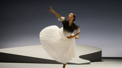 Tänzerin in schwarz-weißem Kleid bewegt sich auf grauer Bühne