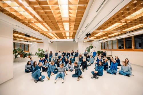 viele Menschen in einem großen Raum, alle tragen blaue Kleidung und sitzen in verschiedenen Positionen auf dem Boden