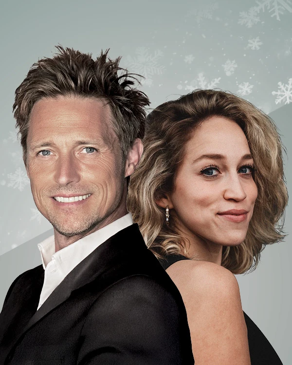 Zwei Personen stehen Rücken an Rücken in festlicher Kleidung vor einem winterlich dekorierten Hintergrund mit Schneeflocken. Die Gesichter sind unscharf, wodurch keine Identifikation möglich ist.