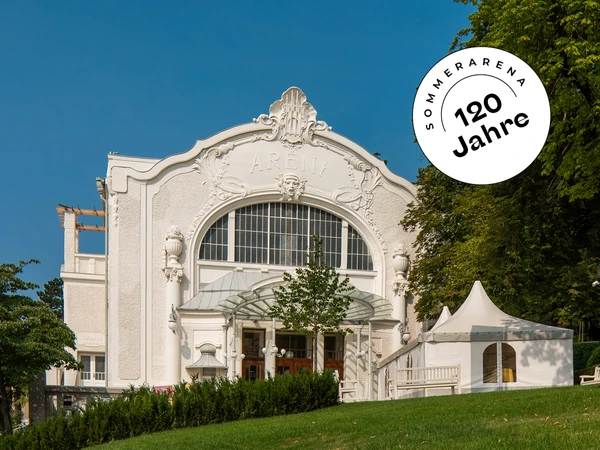 Das Foto zeigt ein historisches Gebäude im Jugendstil mit der Aufschrift „ARENA“ über dem Haupteingang. Die Fassade ist reich verziert mit geschwungenen Ornamenten und plastischen Details, typisch für die Architektur des frühen 20. Jahrhunderts.