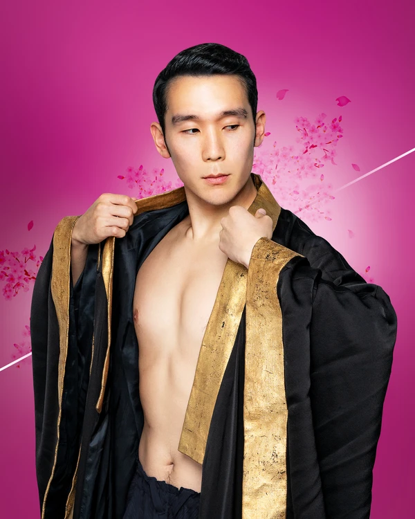A person wearing a black robe with gold trim opens it slightly and looks sideways, set against a pink background with floating petals.