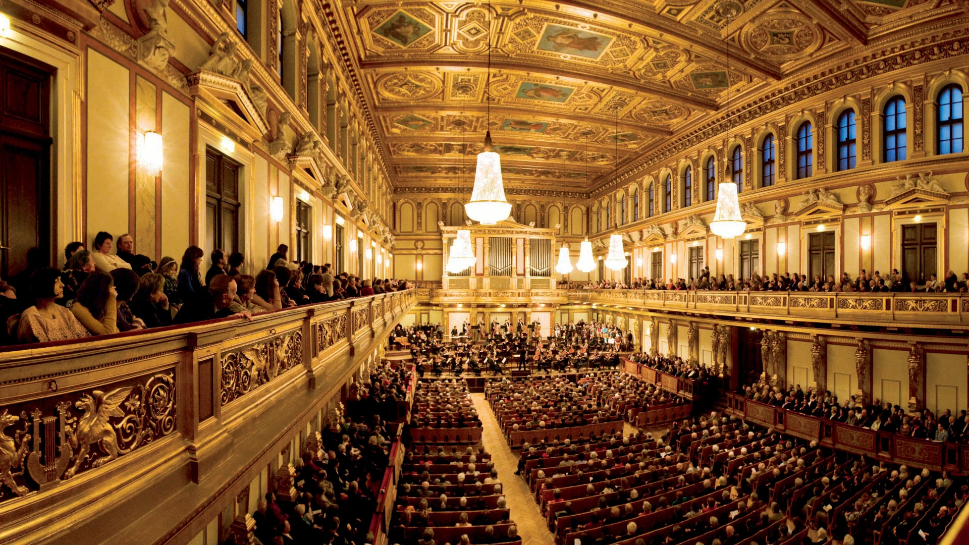 Opulenter Konzertsaal mit reich vergoldeter Decke, großen Kronleuchtern und voll besetztem Publikum.