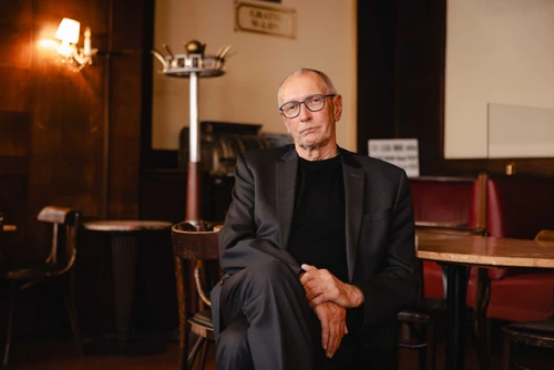 Grauhaariger Mann mit Brille sitzt leger an einem Kaffeehaustisch