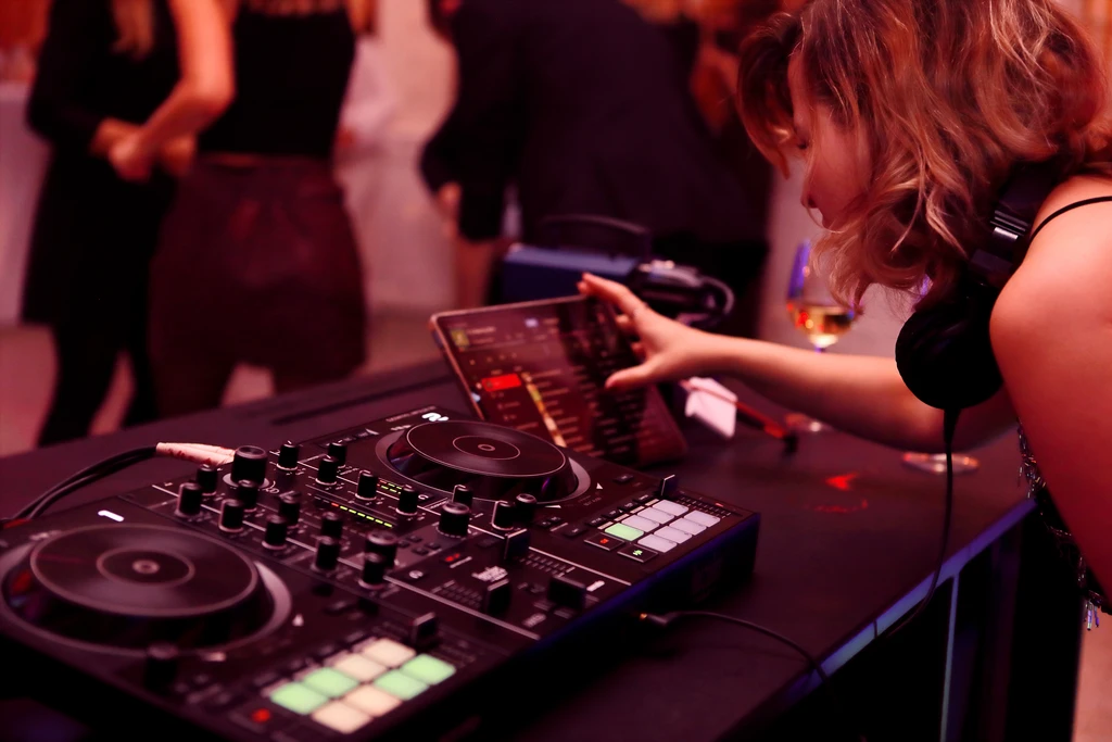 Turntables werden von DJ Rambo Schmidt bedient. Im Hintergrund tanzen Besucher*innen.