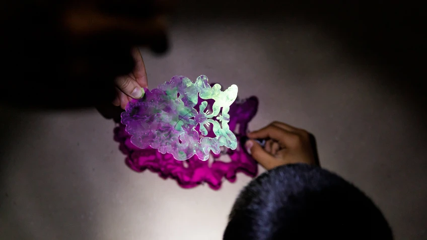 Children's hands hold a cut Plexiglas figure by Robert Gabris that casts a purple shadow on the background.