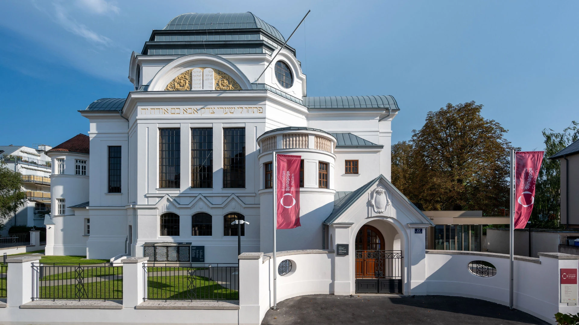 Frontansicht der renovierten Synagoge mit weißer Fassade, Rundbogenfenstern und hebräischer Inschrift.