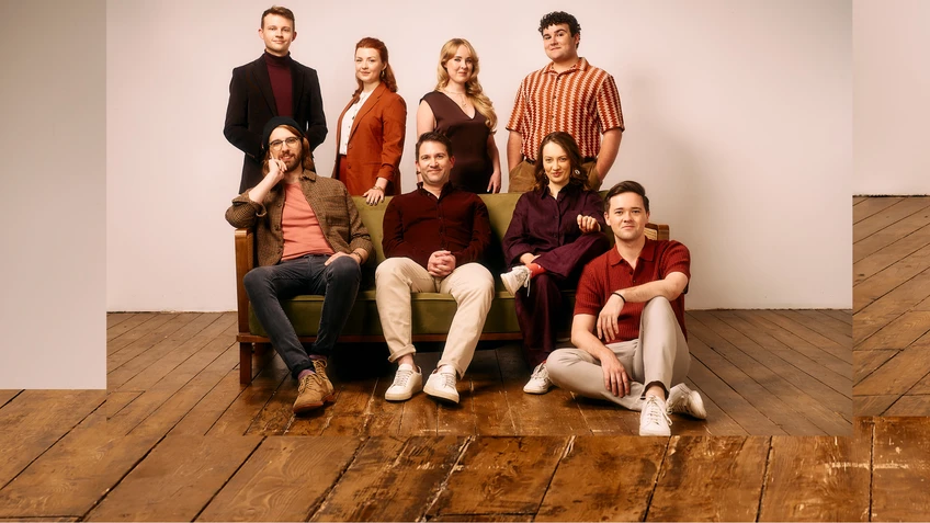 A group photo of the a cappella group VOCES8, casually dressed and gathered on a green and brown sofa.