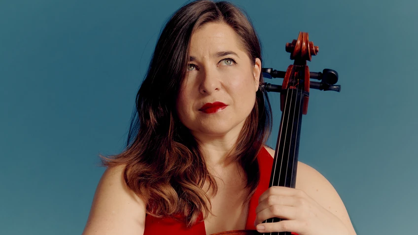 Photo of Alisa Weilerstein, soloist with the violoncello, with her instrument in front of a light blue background.