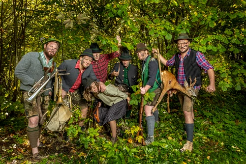 Musikgruppe in Tracht mit Tarnfarbe im Gesicht mit Instrumenten in grünem Gebüsch