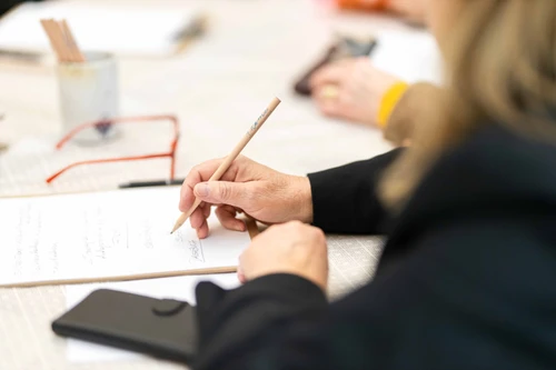 Teilnehmerinnen und Teilnehmer des Schreibworkshops „Just Write“ beim kreativen Schreiben im Museumsraum ausgestattet mit Schreibutensilien wie Klemmbrett und Bleistift