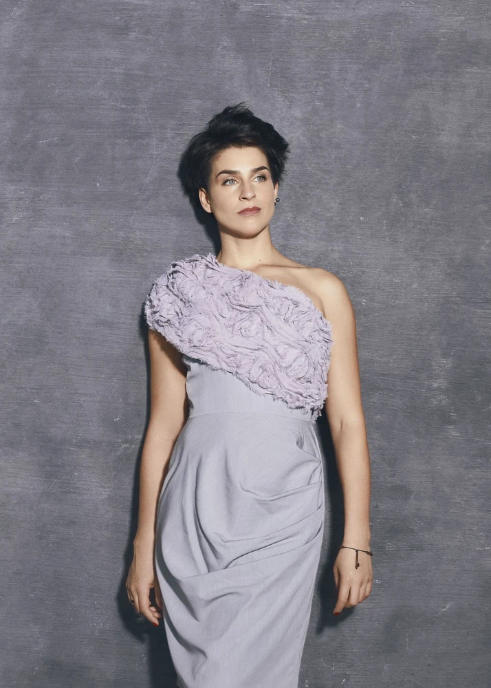 Frau in elegantem hellviolettem Kleid vor einer grauen Wand