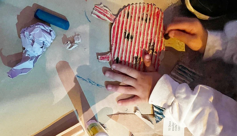 Children's hands making and painting a ladybird out of cardboard.